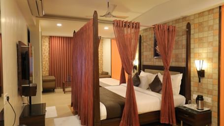 A wide view of a Krushnai Resort bedroom with a four-poster bed, dark wood furniture, and warm lighting.