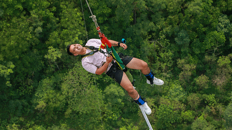 A person bungee jumping against a backdrop of dense forest.