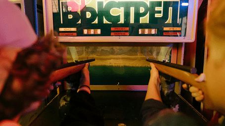 Two people with guns aiming at a screen in front of them.