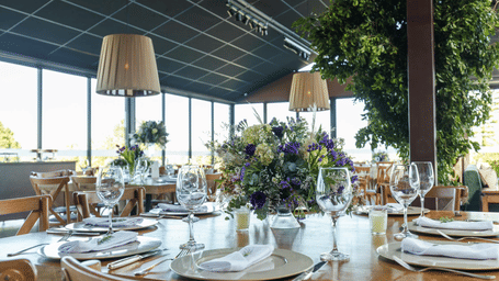 A banquet hall setting with round tables adorned with fine tableware and floral centrepieces under stylish lampshades