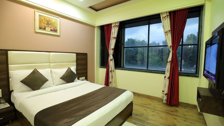 An Executive Room at Krushnai Resort with a white bed, brown accents, and a window with red curtains.