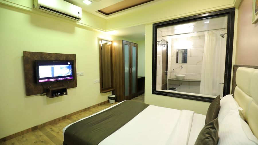 A bedroom at Krushnai Resort with a wall-mounted TV, a bed, and a glass-enclosed bathroom.