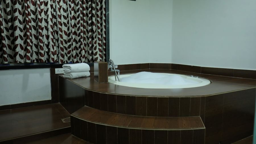 A corner of a washroom in a suite of Krushnai Resort showcasing a large, Jacuzzi with surrounding wooden steps.