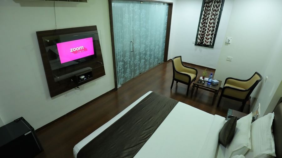 A top angle of a bedroom at Krushnai Resort with a bed, two chairs and a wall-mounted television.