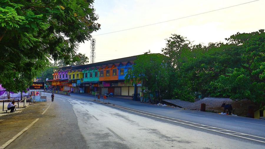 The Krushnai Resort building with colourful facades lines a quiet road, framed by green trees under a bright sky.