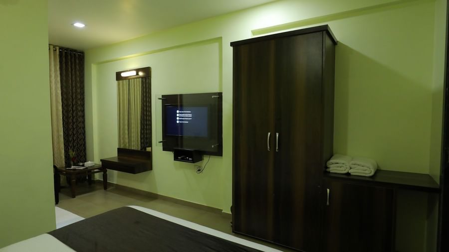 A clean and well-lit bedroom at Krushnai Resort featuring a dark wooden wardrobe and a TV.