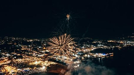 A firework bursts over a cityscape at night, illuminating the urban scene with a bright display.