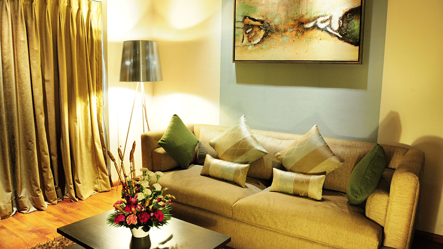 A comfortable couch with cushions arranged on it with a tall lamp brightly illuminating the living area of the Premier Suite - Senses Hotel
