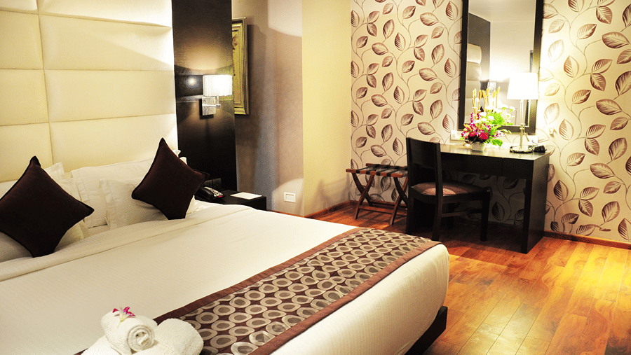 A wide angle shot of the bedroom of the Premier Suite featuring a double bed with soft cushions kept on it - Senses Hotel