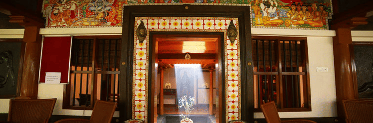 A traditionally decorated entrance at Ayur Ashram, featuring vibrant mural art, wooden interiors, and warm ambient lighting at Uday Samudra Leisure Beach Hotel