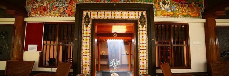 A traditionally decorated entrance at Ayur Ashram, featuring vibrant mural art, wooden interiors, and warm ambient lighting at Uday Samudra Leisure Beach Hotel