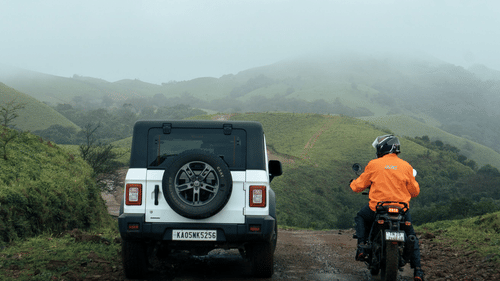White SUV and a biker riding along a misty hill road on the Bangalore to Chikmagalur road trip.