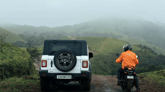 White SUV and a biker riding along a misty hill road on the Bangalore to Chikmagalur road trip.