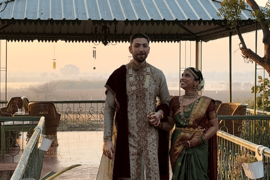 A couple dressed in elegant traditional Indian attire walks hand-in-hand under a garden gazebo structure at Umaid Palace.