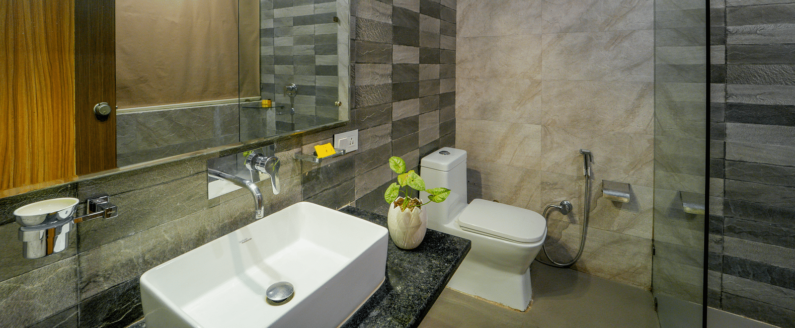 The wash room of the premium room with a wall mounted mirror, wash basin, and the toilet seat - DLS Whispering Winds