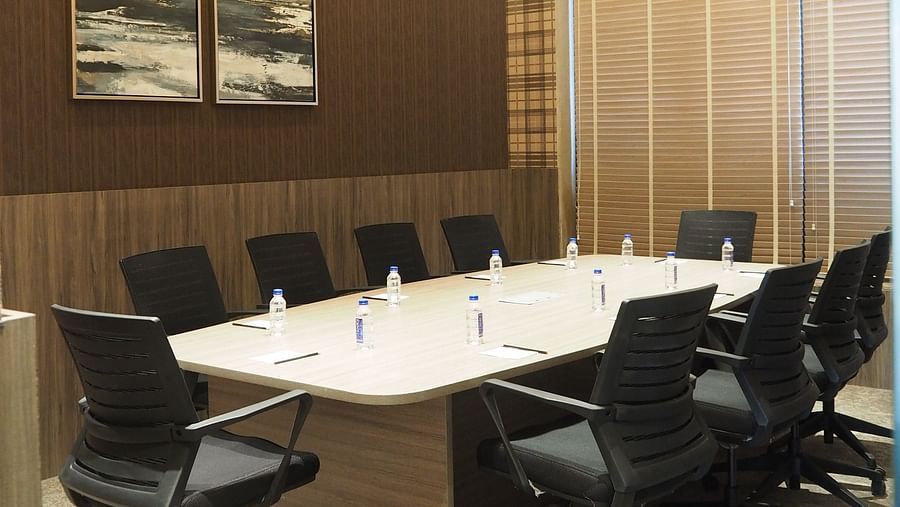 A meeting table with multiple chairs with a dark wall agianst it with a framed picture - Club Charholi, Pune 