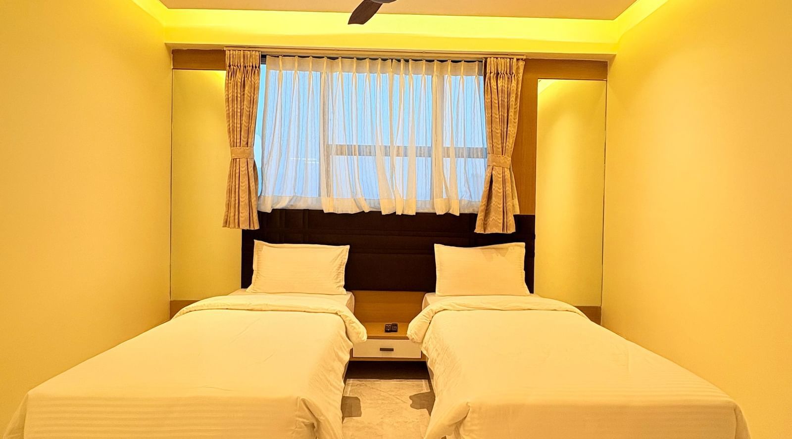 Twin beds in a bedroom with a ceiling fan above at Hotel Mumbai House, Vashi.