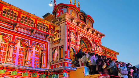 The brightly coloured and ornate facade of the Badarinath Temple in Uttarakhand shows pilgrims gathering at the entrance against a clear blue sky.