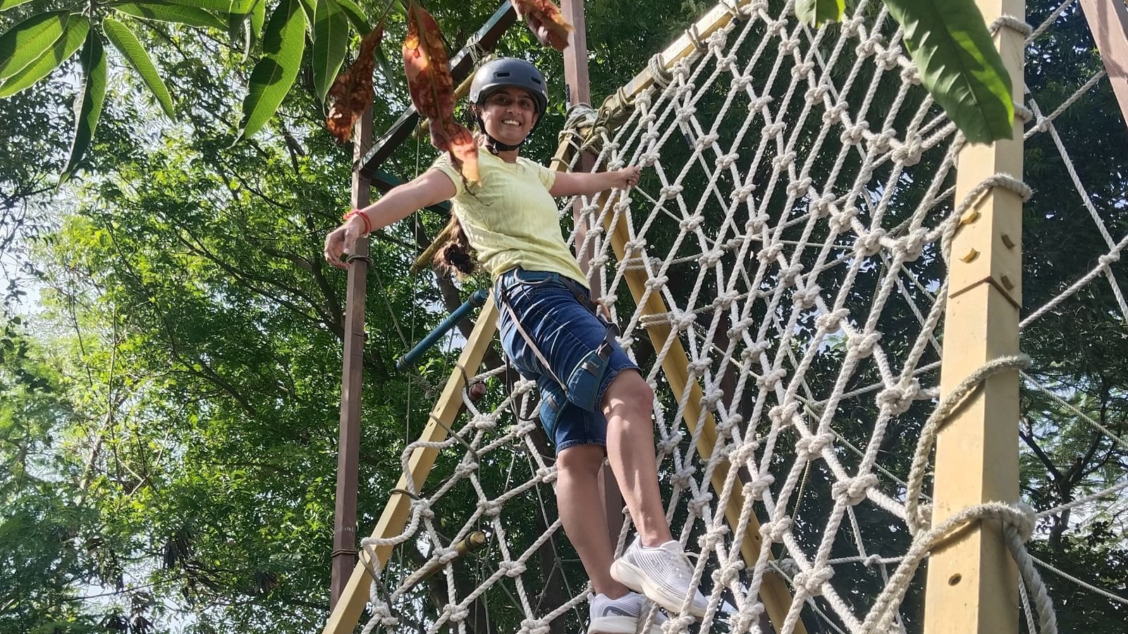 A person climbing the Commando Net surrounded by lush greenery at Daksh Resort & Amusement Park.