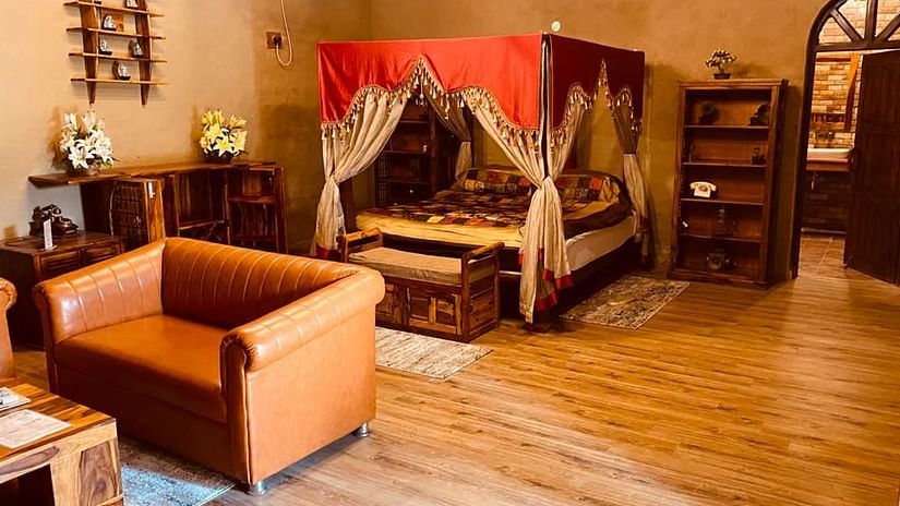 An image of a bedroom with poster bed decorated with fabric pieces, and there is also a seating area consisting of sofa and a table - Themis Mudhouse - An Ethnic Resort & Cultural Dining