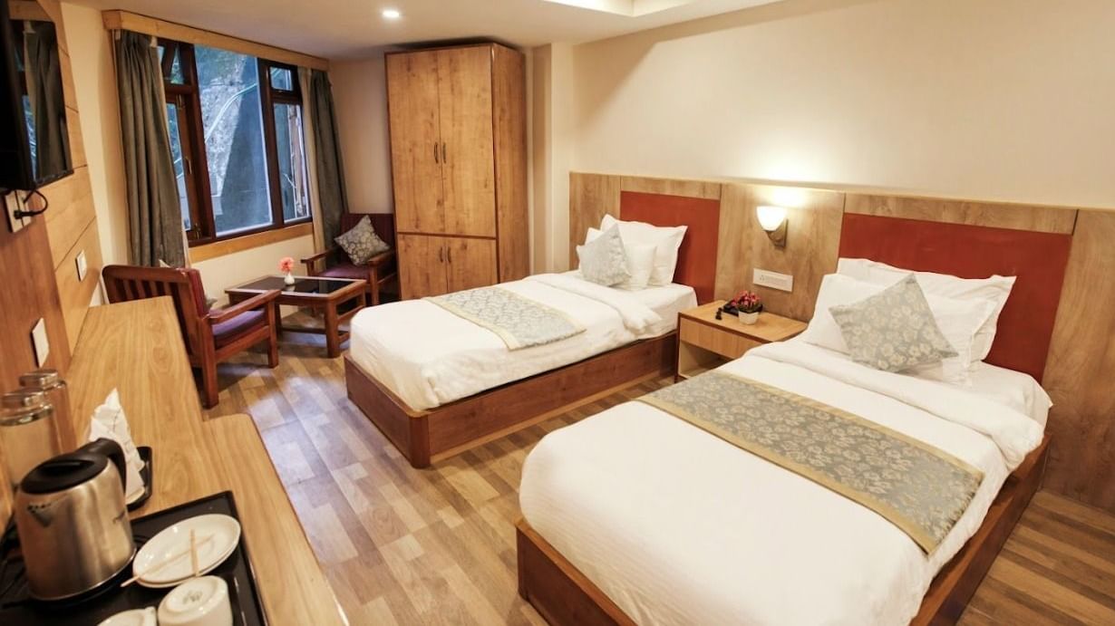 Standard Twin Room at Avianna Gangtok Prime Hotel & Spa featuring a couple of twin beds facing the TV mounted on the wall below which is tea and coffee maker. On one side of the bed is a sitting space next to the window