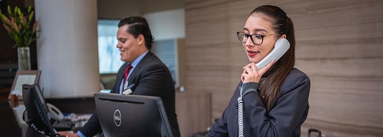 2 staff members standing behind the reception desk with desktops in front of them.
