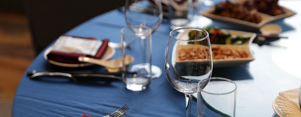 Close up shot of a round dining table with a blue table cloth over it along with well arranged cutlery.