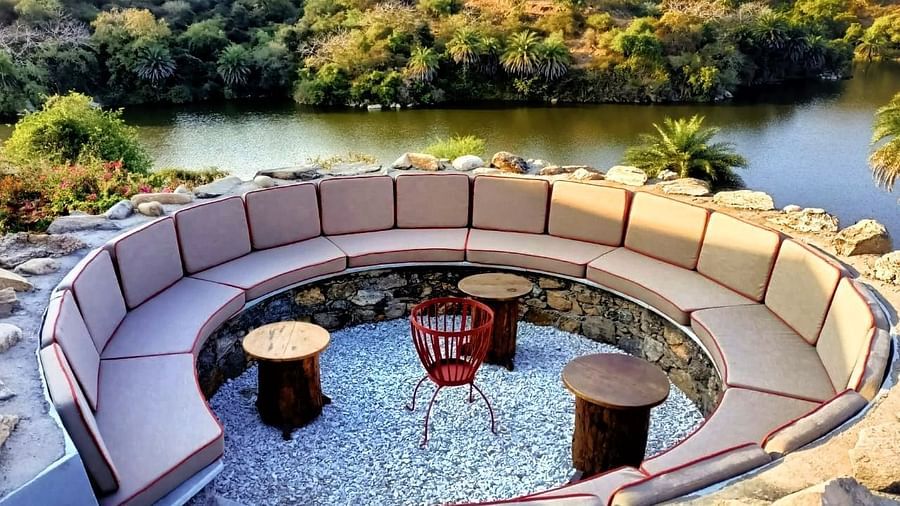 a round sofa with three small tables in front of it and the lake and forest in the background - Chunda Shikar Oudi, udaipur