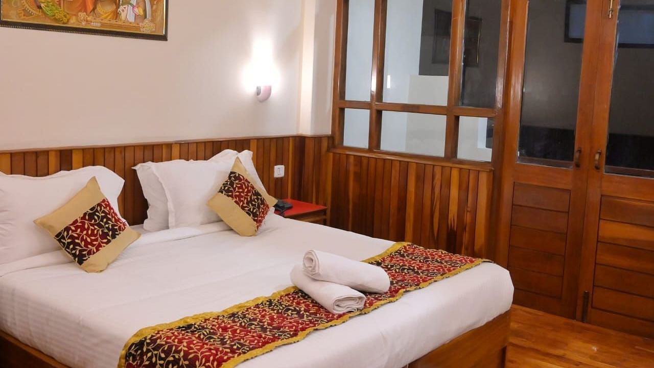 An image of the super deluxe room featuring a queen size bed, bed side table, lamps, and an expansive door leading to the balcony - Ecotel Chiminda, Pelling