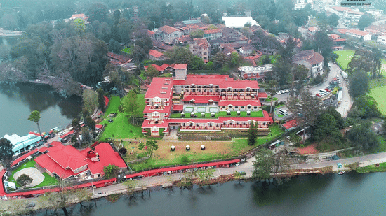 Aerial view of The Carlton Kodaikanal with red-roofed resort buildings, lush greenery, and a serene lake surrounding the property.