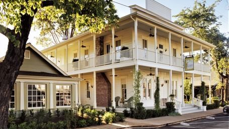 Corner view of Tallman Hotel showing 2-storey floor with wraparound balconies surrounded by greenery