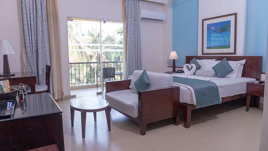 Complete view of the Deluxe room with a double bed, a couch a small tea table and a balcony at Kyriad Prestige Calangute, Goa