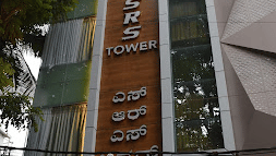 Full view of the building of SRS Suites, Koramangala, surrounded by lush green trees.