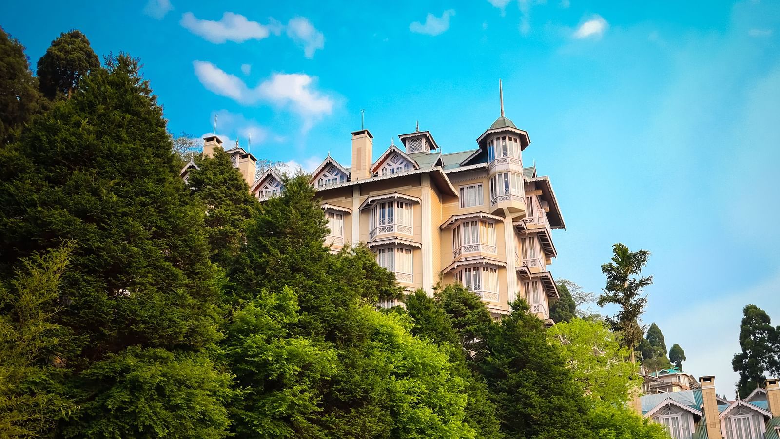 Cedar Inn, Darjeeling nestled amid lush green trees, showcasing its charming colonial architecture against a clear blue sky in the Himalayan foothills.