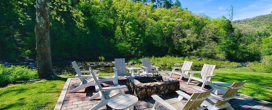 an outdoor seating area with a fire pit in the middle surrounded by wooden chairs amidst lush greenery - Historic Tapoco Lodge