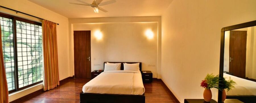 A spacious bedroom in Aqua Bungalow with warm lighting and wooden flooring at Vedic Village Spa Resort.
