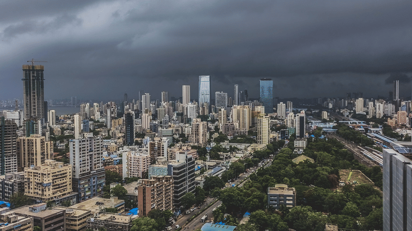 Dark storm clouds gather over a sprawling modern city with tall skyscrapers and green parks below.