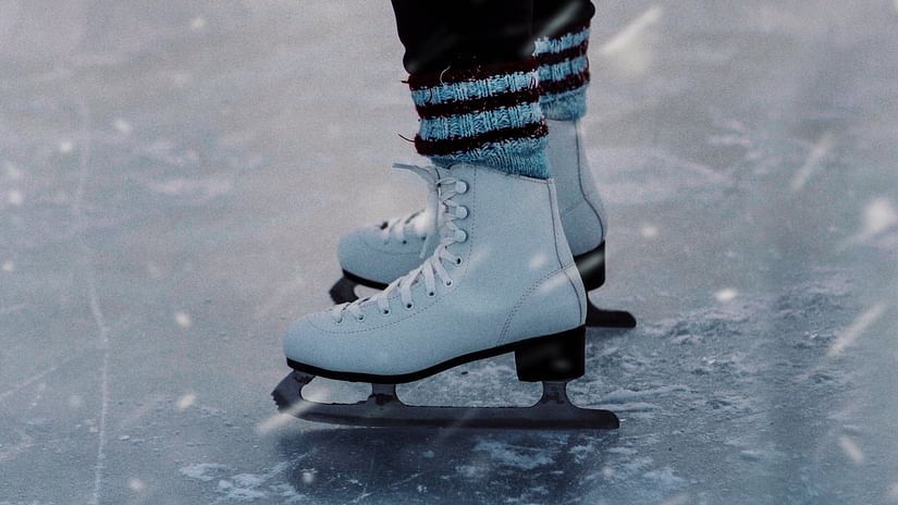 A close shot of the feet of an ice skater wearing ski boots on ice.
