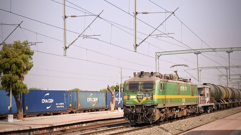A passenger train passing through a platform with overhead electric lines.