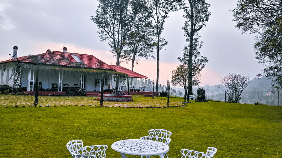An overview of a lawn area with metal chairs and table and Ibex Resort, Coonoor (Leewood) in the background.