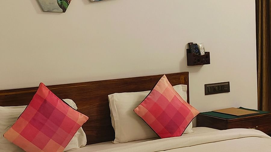 Front view of a double bed with two pink pillows kept on it and hexagonal frames hanging on the wall in 101 non-ac room at Ananda Holiday Home, Wayanad 1