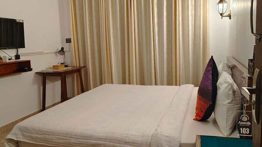 Side view of the double bed in 103 room along with cream coloured curtains on the window at Ananda Holiday Home, Wayanad 8