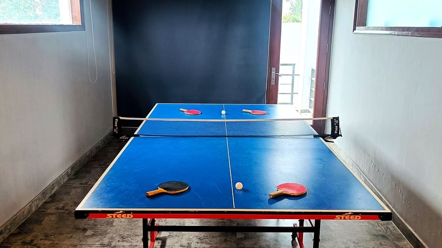 A table tennis setup featuring two bats and a ball on each side, set in a brightly lit room at DLS Forest Vines Resort & Spa, Ramnagar (Jim Corbett).