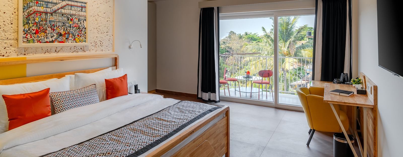 Bright hotel room with, flat TV screen, work desk and chair, vibrant art on the wall, and an access to the balcony at Bedzzz Xclusiv Morjim, Goa