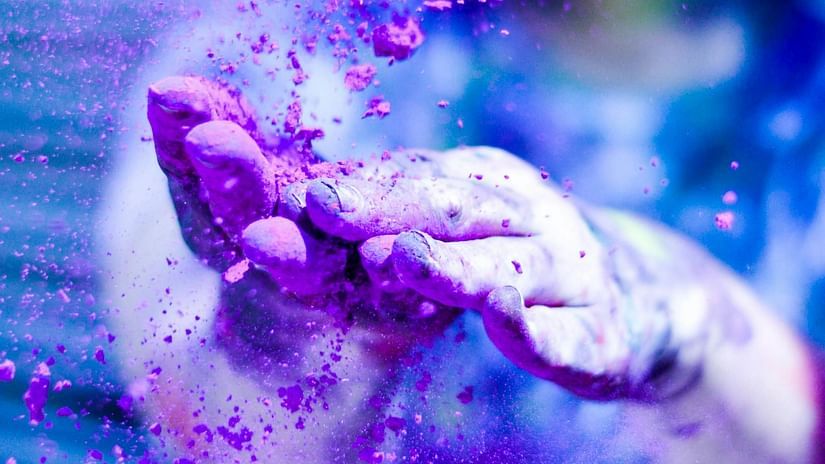 Hands joyfully throwing vibrant purple powder during the Holi festival celebration.