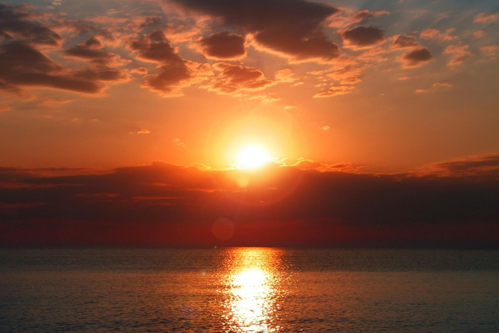 A beautiful sunset with the sun rays reflecting on the ocean bed along with a cloudy sky in the background.