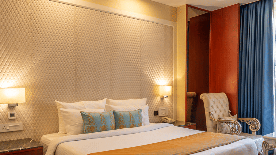 Luxurious bedroom with exposed dark wooden ceiling beams, a large bed, and intricate textured wall behind the headboard at Hotel Hukam's Lalit Mahal.