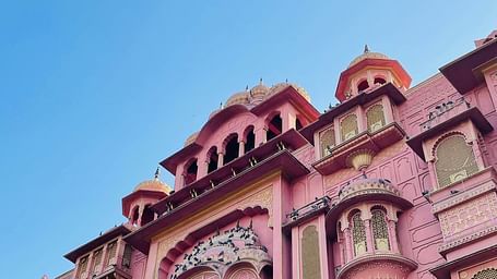 A grand, ornate pink palace with intricate architecture and arched windows, under a clear blue sky.