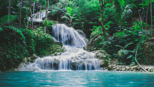 A serene multi-tiered waterfall flowing into a turquoise pool, set against a lush green backdrop.