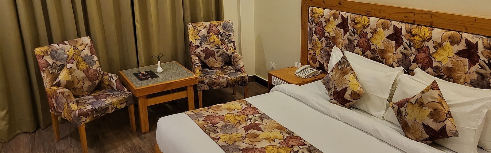 Side angle of the bedroom, featuring comfortable seating, elegant curtains, and wooden flooring at Dagshai Manor Kasauli - Inde Hotels.